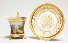 A BERLIN PORCELAIN CUP AND SAUCER, the cup on claw feet and painted with a classical landscape.