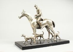 A SILVERED BRONZE GROUP HORSE AND RIDER, with their dogs, on a wooden base. 17ins long, 12ins high.