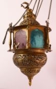 A GOOD BRASS QAJAR HANGING LAMP, with coloured glass panels, bird finial, the actual lamp