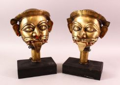 A PAIR OF 19TH / 19TH CENTURY SOUTH INDIAN BRASS MASKS OF SHIVA, each mounted on wooden bases,
