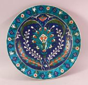 A TURKISH OTTOMAN IZNIC STYLE POTTERY PLATE, with a blue ground and floral decoration 30cm