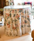 A GLASS TOP CIRCULAR TABLE with floral fabric. 2ft 8ins diameter.