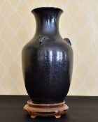 A CHINESE POTTERY VASE with rams mask handles. 15ins high, on a wooden stand.