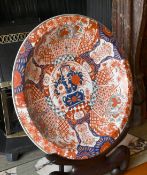 A LARGE JAPANESE IMARI DESIGN CIRCULAR CHARGER on a wooden stand. 2ft diameter.