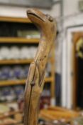 A folk art walking stick modelled as a snake eating a bird