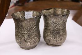 A pair of Eastern white metal beakers with embossed decoration