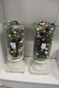 A pair of glass and pottery vases containing a large collection of marbles