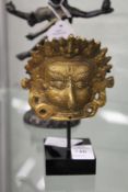 A small Tibetan gilt bronze mask on stand