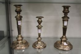 A pair of plated candlesticks and similar smaller candlestick