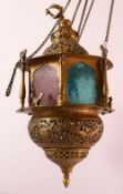 A GOOD BRASS QAJAR HANGING LAMP, with coloured glass panels, bird finial, the actual lamp