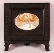 A GOOD INDIAN CARVED EBONY & PAINTED frame, the frame carved with native foliage, the centre with