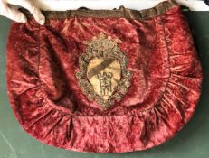 AN INTERESTING CRIMSON VELVET HANDBAG, applied with an earlier gold thread embroidery armorial badge