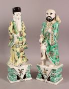 A PAIR OF CHINESE FAMILLE VERTE PORCELAIN IMMORTAL FIGURES, each figure holding a staff or stick,