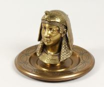 AN EGYPTIAN REVIVAL BRASS INKWELL, modelled as a bust of a pharaoh, on a circular base. 7.5ins