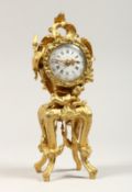 A GROUP SMALL 19TH CENTURY FRENCH GILT METAL CLOCK on a stand with putti and garlands. 8.5ins high.