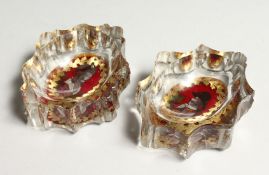 A PAIR OF CUT GLASS SALTS, with cranberry tinted and gilt decorated portraits to the bases. 3ins