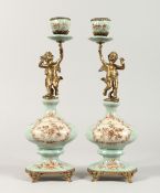 A PAIR OF CONTINENTAL PORCELAIN CUPID CANDLESTICKS on gilt bases. 14ins high.