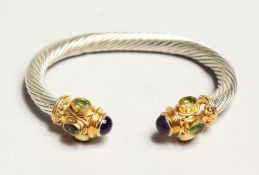 A TWISTED SILVER TORQUE STYLE BANGLE, set with a pair of cabochon amethysts and six oval peridots.