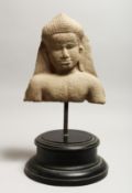 A CAMBODIAN CARVED STONE FRAGMENTARY BUST, mounted on a circular base 18ins high.