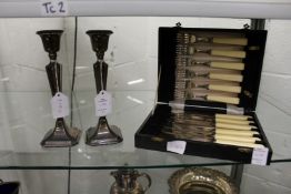 A pair of silver candlesticks and a cased set of plated fish knives and forks.