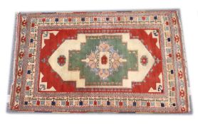 A TURKISH WOVEN WOOL RUG, early 20th Century with a central pale green ground panel and stylised