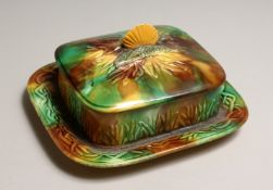 A MAJOLICA SARDINE DISH AND COVER, green and brown glaze with moulded decoration and shell handle.