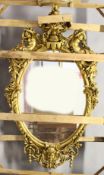 A LARGE IMPRESSIVE GILT FRAMED OVAL MIRROR, the frame mounted with a cherub seated on an urn, with
