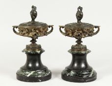 A PAIR OF BRONZE TWO HANDLED URNS AND COVERS on circular marble bases. 10ins high.