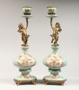 A PAIR OF ORNATE PORCELAIN AND ORMOLU CANDLESTICKS with cherub supports. 14ins high.