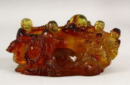 AN AMBER STYLE GROUP OF LAUGHING BUDDHA, surrounded by children, 20cm long.