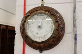 A circular aneroid barometer with carved oak frame.