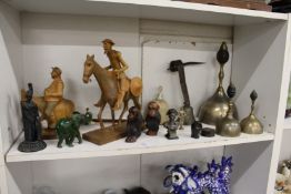 A shelf of decorative ornamental items to include brass bells, carved wood figures etc.