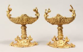 A PAIR OF GILT BRONZE CLASSICAL STYLE PEDESTAL TABLE SALTS. 9ins high x 7ins wide.