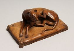 AFTER GOTT. A CARVED WOOD FIGURE OF A DOG on a cushion 6ins long.