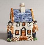 A 19TH CENTURY PRATTWARE MODEL OF A COTTAGE, with a male figure standing to each side. 4ins wide x
