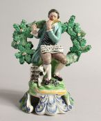 A PRATT WARE BOCAGE GROUP OF A SEATED MAN dog at his side playing a flute. 6ins high.