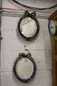 A pair of continental porcelain encrusted oval mirrors with cherub crestings.