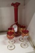 A good cranberry coloured and gilt decorated liqueur set comprising a decanter (lacking stopper) and