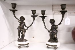 A pair of ornate twin branch candelabra modelled as cherubs holding two branches, on a marble base.