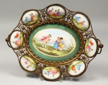 AN ORMOLU DISH, the centre and border inset with porcelain panels painted with children. 15ins long