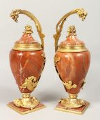 A GOOD PAIR OF RED MARBLE URNS with ormolu mounts and cherubs on square bases. 13ins high.