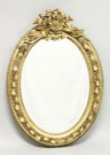 A DECORATIVE GILT FRAMED OVAL WALL MIRROR, the cresting with musical instruments, the frame with