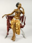 A PAINTED BRONZE GIRL seated in a chair. 18ins high