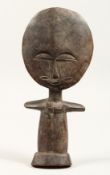 A SMALL TRIBAL FIGURE OF A WOMAN, with a large, disc shaped head. 9.5ins high.