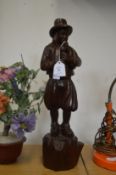 A carved wood figure playing a bladder pipe.