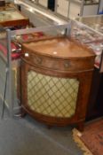 A yew wood bow fronted corner cabinet with a single frieze drawer above a brass grilled door.
