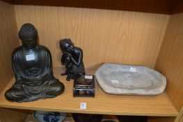 Two figures of Buddha, a stone trough and a cigarette box.