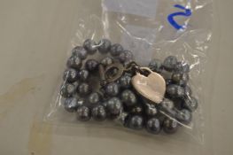 A pearl necklace with silver heart shaped pendant.