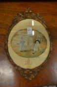 An oval silk work picture of children under a tree, in a decorative gilt frame.
