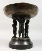 A BRONZE AND SIMULATED MARBLE COMPORT, supported by three bronze cherubs. 9ins diameter.